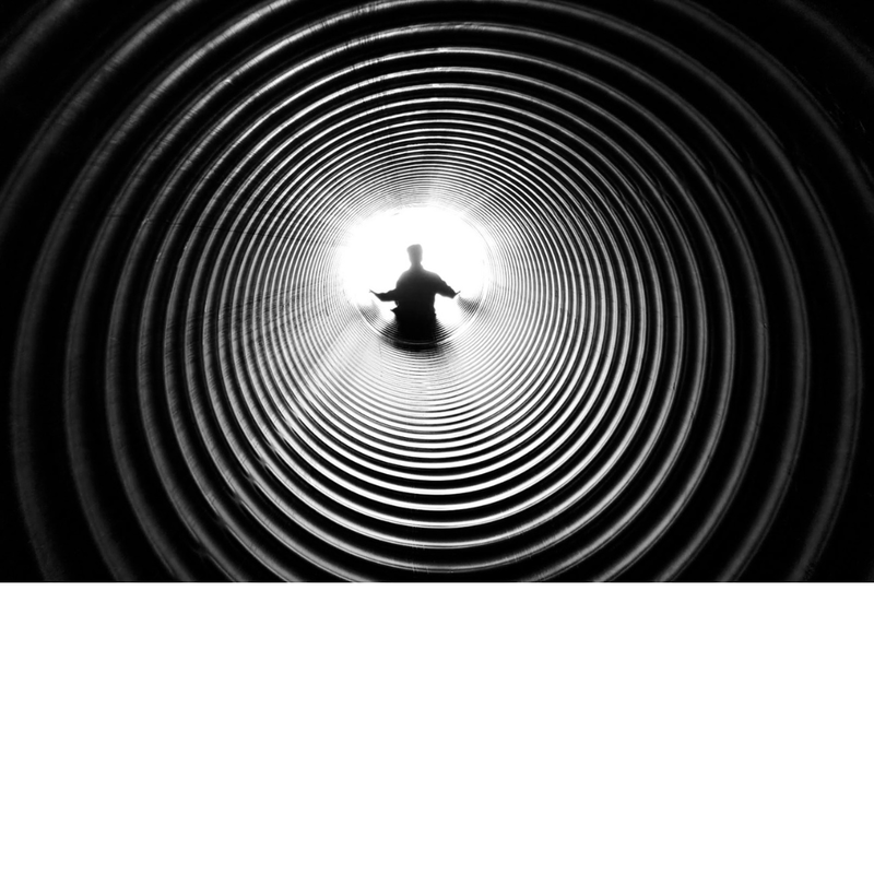 black and white photo looking down a ridged tube toward a backlit person