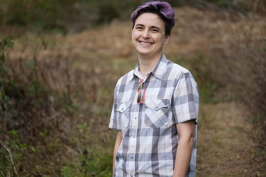 smiling purple-haired person standing on a hiking trail