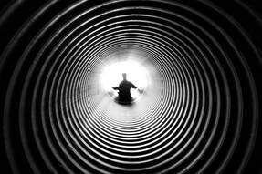 black and white photo looking down a ridged tube toward a backlit person