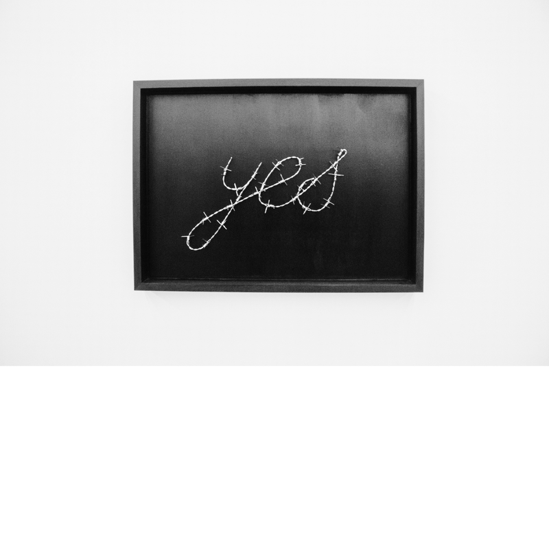 black and white photo of the embroidered word "yes" on a dark background, framed